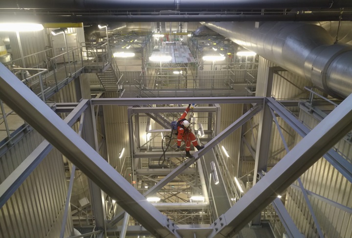 Rope access specialist verwijdert stof op hoogte in fabriek met industriële stofzuiger