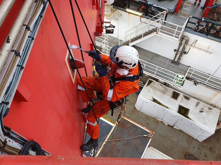 Rope access specialist voert schilderwerk en onderhoud uit op hoogte aan scheepsromp